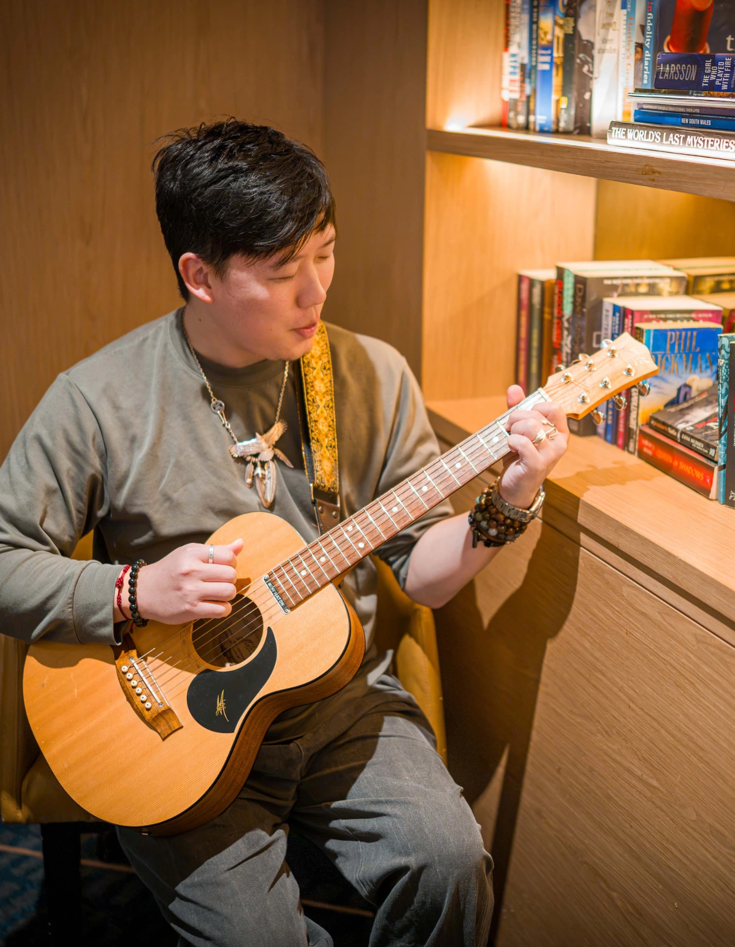 Jeremy Yau, Registered Music Therapist, playing an acoustic guitar beside a bookshelf