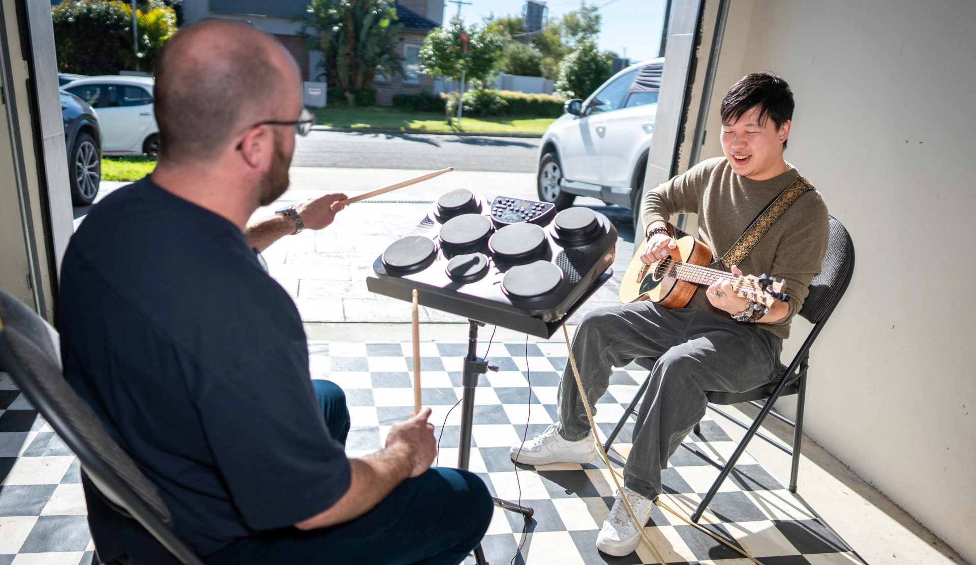 Music therapist playing guitar alongside a client on electronic drums in a bright home clinic space